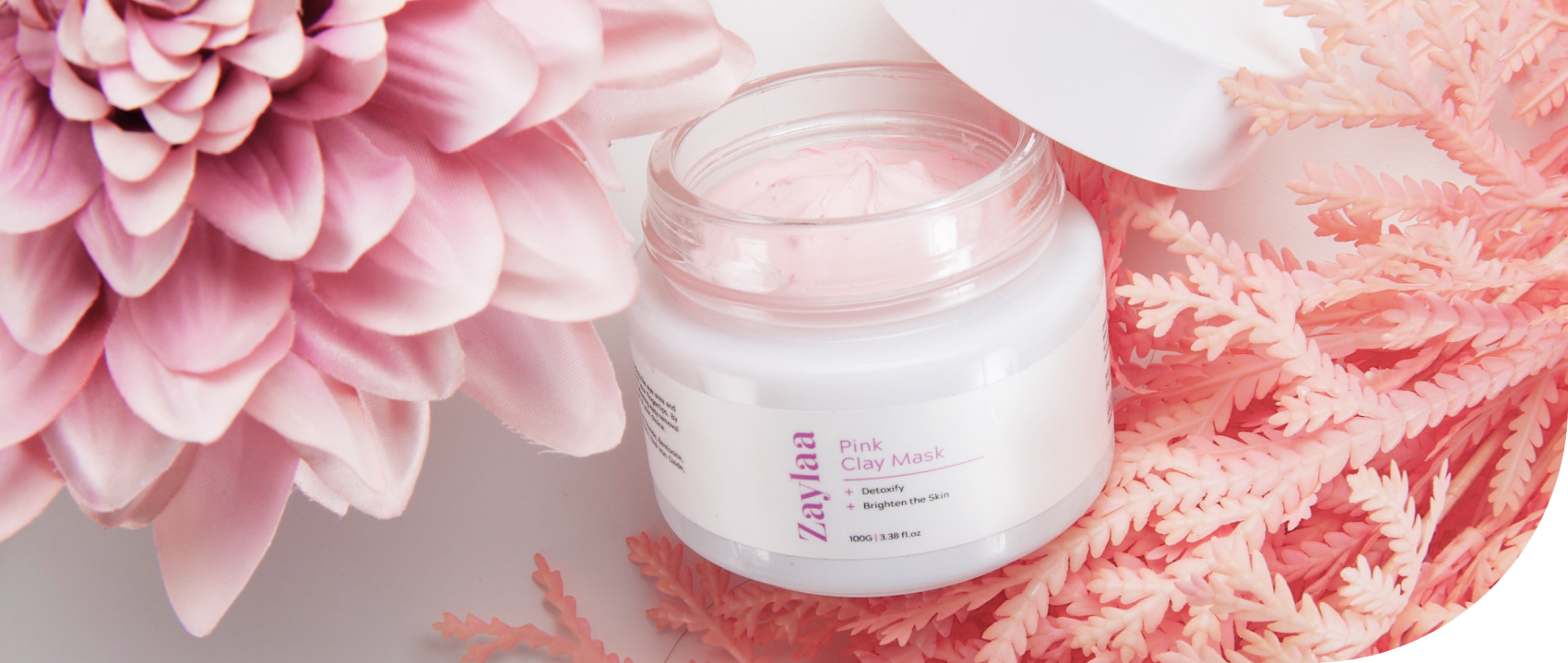 Image of a jar of pink clay mask next to a pink flower