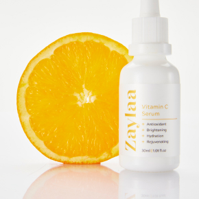 A bottle of Zaylaa vitamin C serum next to a sliced orange on a white background.